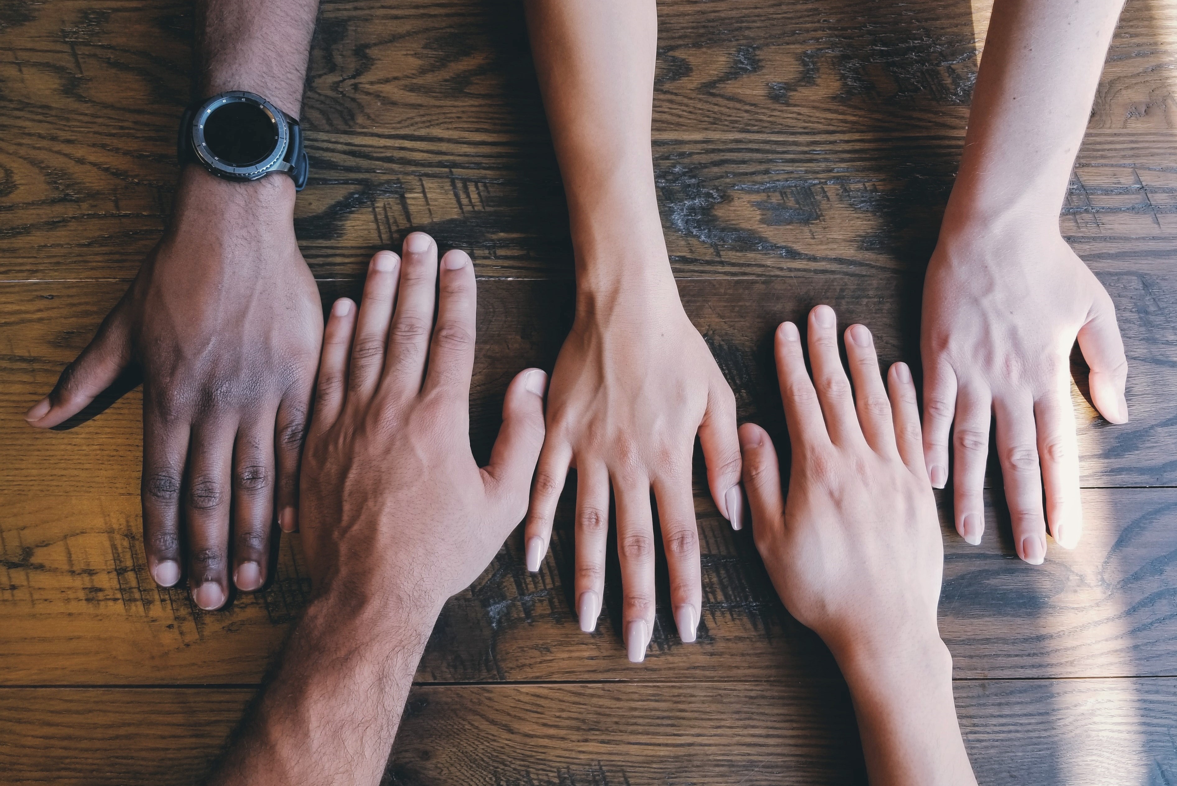 hands from a diverse group of people come together on a wooden table